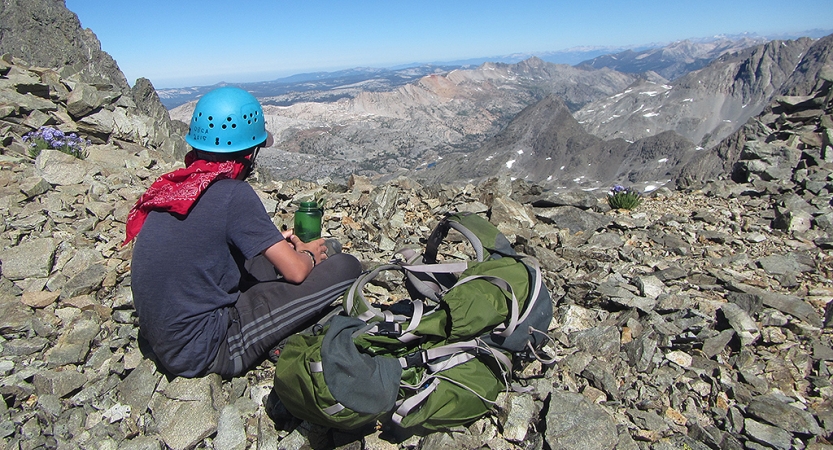 a person wearing a helmet rests on a rock and looks out over a vast rocky landscape